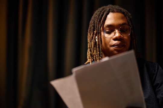 African American young adult student reading printed notes, reviewing coursework with focused expression. Education concept for academic success, exam prep, online learning promotion
