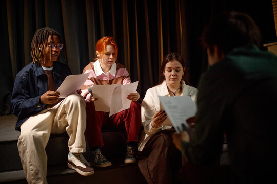 Students rehearsing from printed scripts during group acting class on stage, building teamwork and performance skills. Useful for education, youth theater, creative learning
