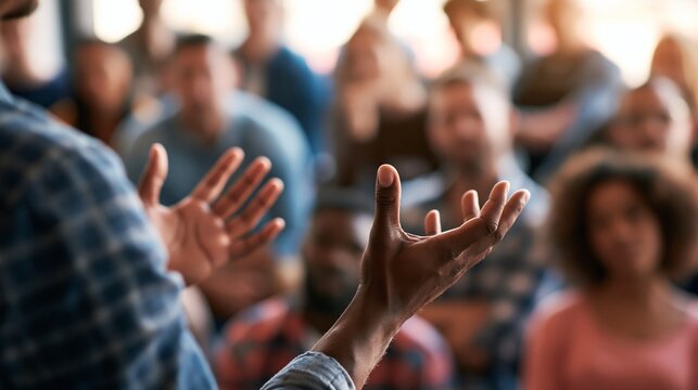 Dynamic mediumwide eyelevel view of a persuasive speaker using open palm gestures during a community forum highlighting the speaker sharply against a softly blurred backdrop of