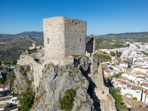 Aerial view of the historic Castillo de Olvera perched on a rocky cliff overlooking the white-washed village and rolling hills under a clear blue sky in Olvera, Andalusia, Spain.