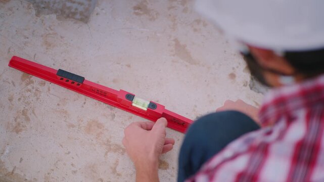 Over shoulder shot of a construction worker using a spirit level to check the floor level at a construction site.