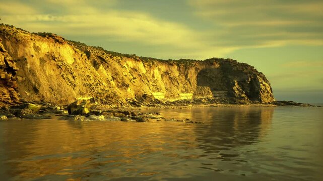 dramatic cliff face glowing in gold, closeup view of textured strata and steep rock, warm cinematic lighting casts deep shadows and highlights rugged details