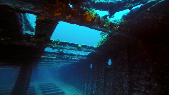 Endless Shipwreck Interior Exploration at 40m Depth Slow Motion. The camera captures a high-contrast scene between the bright blue ocean light and the dark, unlit iron beams of the upper deck skeleton