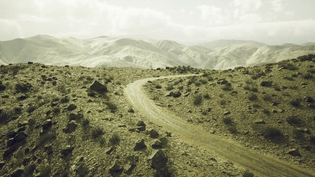 Curving gravel track across barren ridge, soft dawn light, layered mountain silhouettes, thin mist in valleys, ochre tones, expansive steppe and rugged horizon,