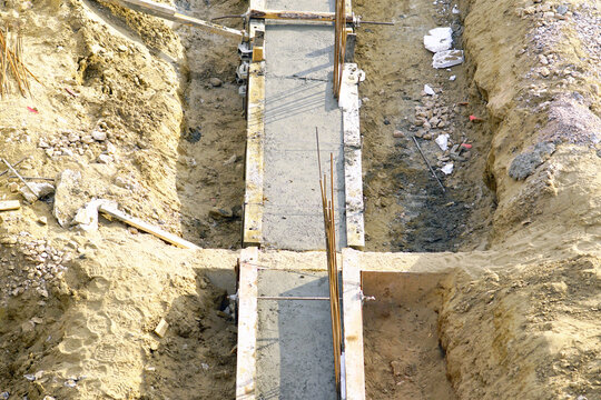 Narrow poured concrete corridor extending through excavated earth cut at active civil engineering site. Shows directional foundation forming, longitudinal trench organization, and structural alignment