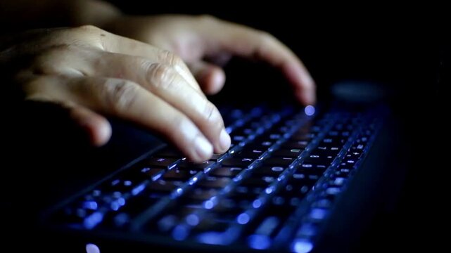 Close-up of a woman's hands typing on laptop keyboard at night working late in dark room. The woman typing business email on laptop device late at night concept of freelance job and flexible working