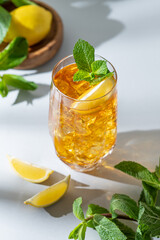 Fototapeta premium Iced tea with lemon and mint in a glass on a light background with shadows