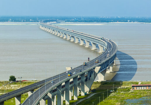 Aerial view of Padma Bridge spanning across the wide Padma River with vehicles driving along the road under a clear blue sky in Mawa, Dhaka Division, Bangladesh.