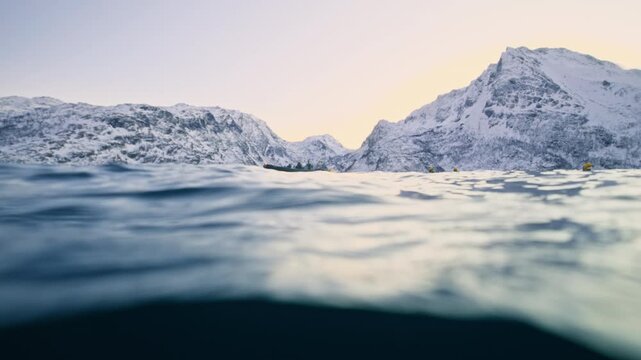 Split-level ocean beneath snowy Arctic mountains and calm fjord water in Norway, zodiac inflatable boat on horizon