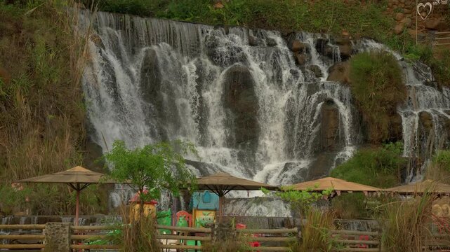 Static shot of Tad Khoo waterfall in Laos, with umbrellas and colourful playset in the foreground.