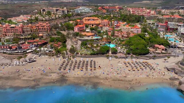 Aerial view gliding over sandy Playa del Duque beach with umbrellas and resorts