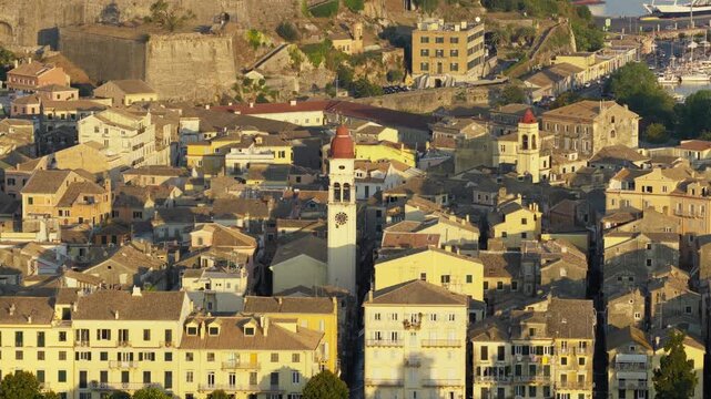 Slow orbit drone shot of Saint Spyridon Church, Corfu Old Town at sunrise. Golden morning light on iconic bell tower