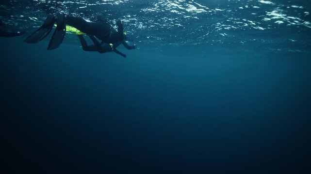 Freediver gliding beneath Arctic Norway fjord surface in dark blue water