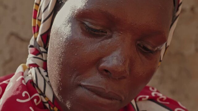 Close-up portrait of an African woman washing clothes with limited water, highlighting water scarcity, resilience, daily household work and rural village life.
