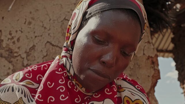 Close-up portrait of an African woman washing clothes with limited water, highlighting water scarcity, resilience, daily household work and rural village life.