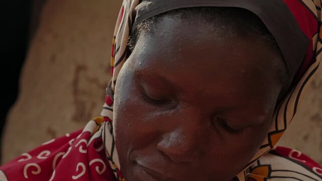 Close-up portrait of an African woman washing clothes with limited water, highlighting water scarcity, resilience, daily household work and rural village life.