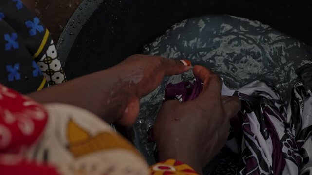 Close-up of hands washing clothes in soapy water outdoors, showing traditional laundry work, daily household chores and authentic rural life in an African village.