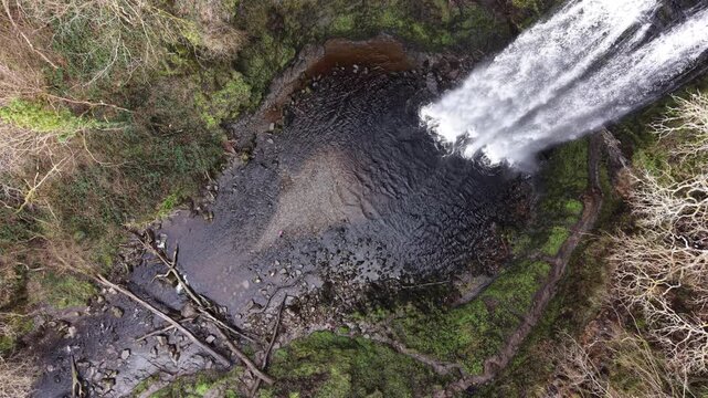 4K drone footage showing Henrhyd Waterfalls flowing into a deep woodland gorge in natural daylight.
