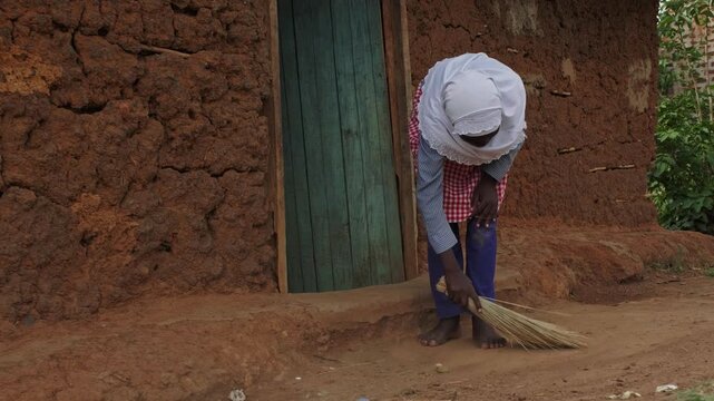 African girl sweeping the ground outside a traditional mud house, showing daily household chores, family support and authentic rural village life in Africa.
