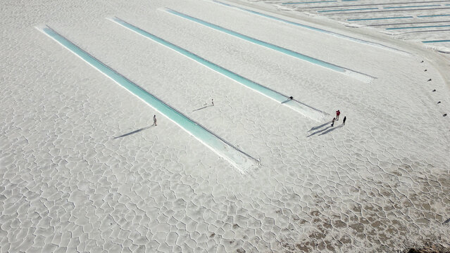 Aerial view of Salinas Grandes salt flats featuring rectangular turquoise pools and people walking across the white salt crust in Tumbaya, Jujuy, Argentina.
