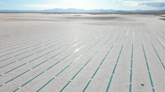 Aerial view of Salinas Grandes salt flats featuring turquoise water channels under a bright sky with distant mountains in Tumbaya, Jujuy, Argentina.