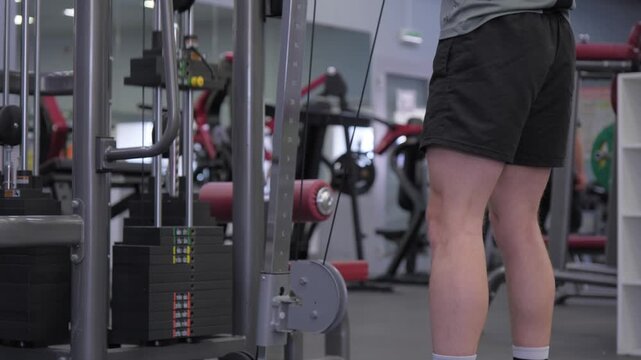 Man lifts weights in a gym while others exercise in the background during daylight hours