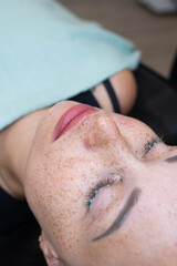 Naklejka premium Close-up portrait of freckled woman during facial spa procedure on teal background