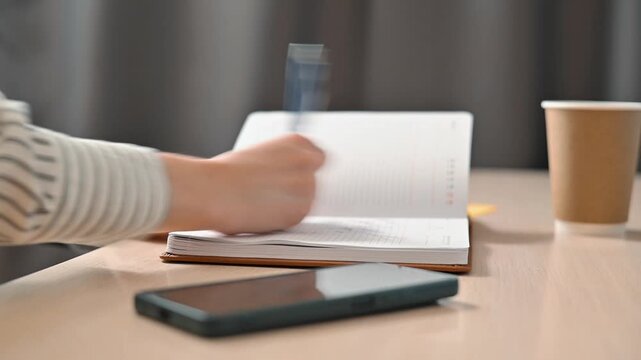 A person is writing notes in a notebook while holding a pen in their hand. A close-up of a hand crossing out written text in an aggressive and angry manner