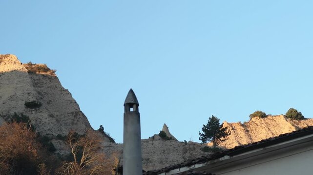 View of the Melnik sand pyramids, with a house chimney in the foreground.

