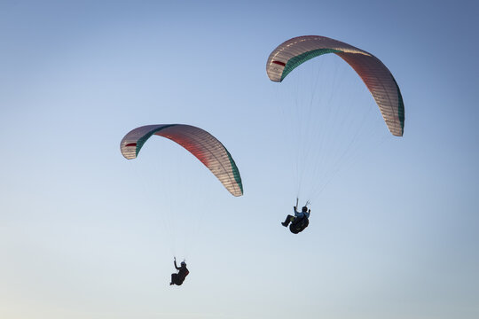 Aerial view of two paragliders soaring through a clear blue sky with soft sunlight over the alpine landscape near Liezen District, Styria, Austria.