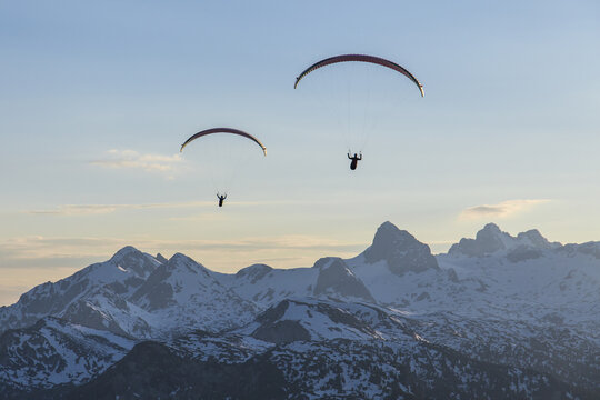 Aerial view of two paragliders soaring over the snow-capped peaks of Hoher Dachstein under a clear blue sky Liezen District, Styria, Austria.