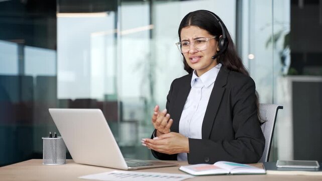 Angry businesswoman in headset arguing over video call using laptop sitting at workplace in office. Frustrated female manager quarrel, having conflict or problem during online business meeting. 