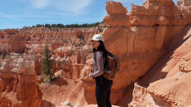 Young smiling woman with a backpack hiking and exploring the scenic navajo loop trail, enjoying the spectacular red rock hoodoo formations of bryce canyon national park in utah on a sunny day