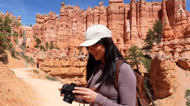 Happy female photographer with a backpack taking pictures of the stunning red rock formations while hiking on a trail in bryce canyon national park, utah, during a sunny summer day