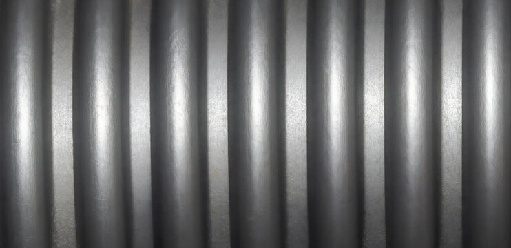 Macro shot of grey flexible corrugated PVC pipe surface. Abstract industrial background of plastic conduit or flexible hose with parallel vertical ribs for cable protection and construction concepts.