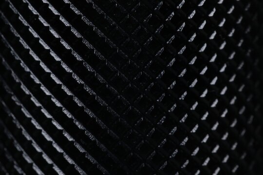 Macro shot of black textured metal surface with diamond knurling pattern. Close up of non-slip ribbed grip texture with selective focus, perfect for industrial, tech, and sports concepts.