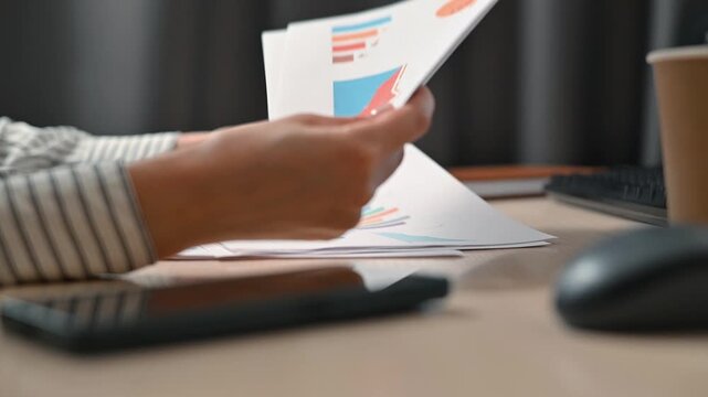 A person performs a review of various business reports at a desk while handling multiple sheets of paper
