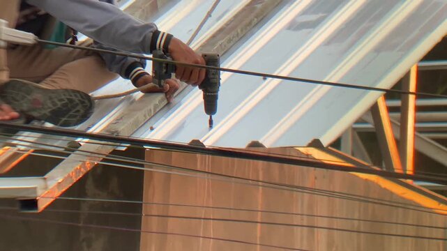 Construction worker installing metal roofing sheets on a building frame using a power drill