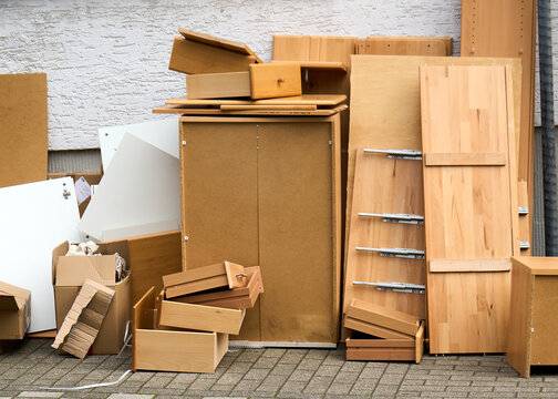 Ein Haufen von ausrangierten Holzm&ouml;beln, Schr&auml;nken, Schubladen und Kartons steht als Sperrm&uuml;ll auf dem gepflasterten Gehweg vor einer wei&szlig;en Hauswand. Konzept f&uuml;r Entr&uuml;mpelung, Umzug oder Wohnungsaufl