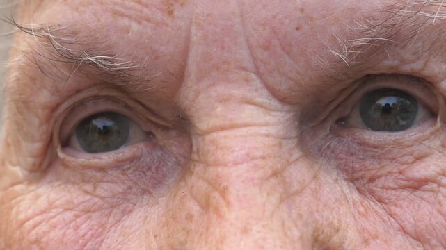 Portrait of grandmother looking into camera with a sad sight. Close up gray eyes of elderly woman with wrinkles around them. Sorrow facial expression of senior lady