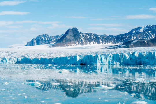View of the Lilliehookbreen glacier featuring a massive blue ice wall and floating icebergs against rugged snow-capped mountains Svalbard, Svalbard and Jan Mayen.