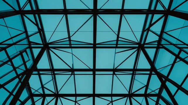 Modern architecture featuring a geometric glass roof and steel structure, creating transparency and reflecting the sky with clouds, highlighting contemporary design and urban infrastructure