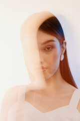 Fototapeta premium Portrait of a young woman with long hair wearing white earrings and a white top. Soft lighting creates a dreamy fashion and beauty concept with artistic blur effects.