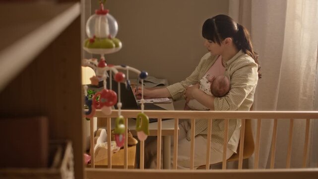 Handheld side view shot of young Caucasian woman sitting at table in nursery room with newborn child in arms and reviewing household bills, managing family budget