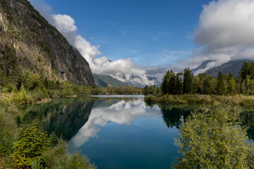 Fototapeta premium Peaceful Alpine Lake Buclet surrounded by mountains under a blue sky and few clouds in the French Alps, Isère