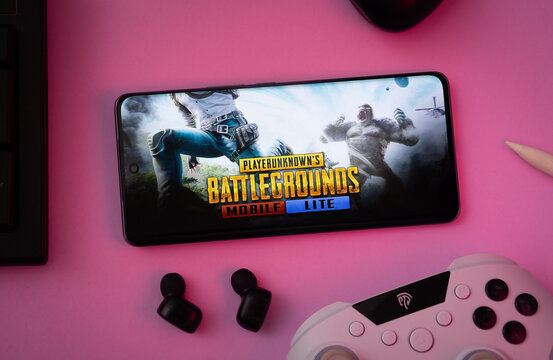 Dhaka, Bangladesh- 23 March 2025: Smartphone displaying PUBG mobile lite game on pink surface with earphones and controller nearby.