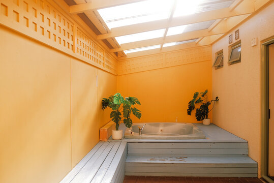 Rotorua, New Zealand: Private guest room courtyard spa patio with a sunken hot tub jacuzzi bath framed by warm yellow walls, sunlight, green plants.