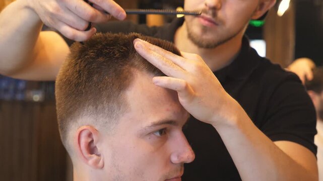 Arms of barber trimming hair of client in salon. Male hands of hairdresser combing and cutting hair of customer with hairbrush and scissors in barbershop. Hairstyling process. Side view Slow motion