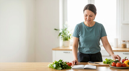 Naklejka na ściany i meble Woman planning a healthy diet with fresh vegetables in the kitchen. Female writing in a notebook for weight loss and nutrition