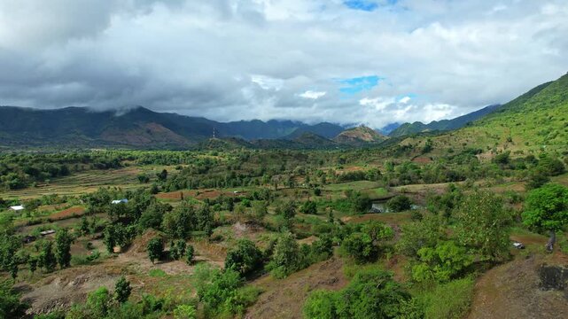 Aerial drone footage of a wild valley in Wera area, easter Sumbawa island, Indonesia, with lot of bushes, trees and plantations, in cloudy weather
